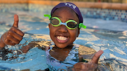 Tween girl in pool holding up two thumbs up while grinning and wearing Green Frogglez Swim Goggles. 