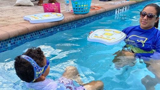 Young boy swimming at swim lessons wearing Blue Wavez Frogglez swim goggles. Looking at swim instructor. Blue neoprene strap with velcro adjusts easily.