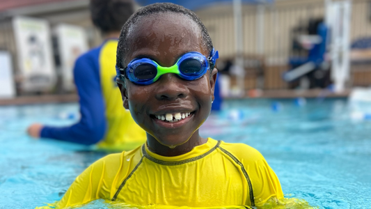 Boy in pool smiling at camera wearing Blue Frogz Frogglez Swim Goggles