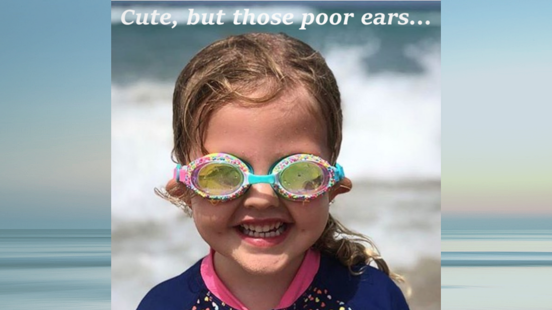 Girl at beach with sand filled goggles pulling ears