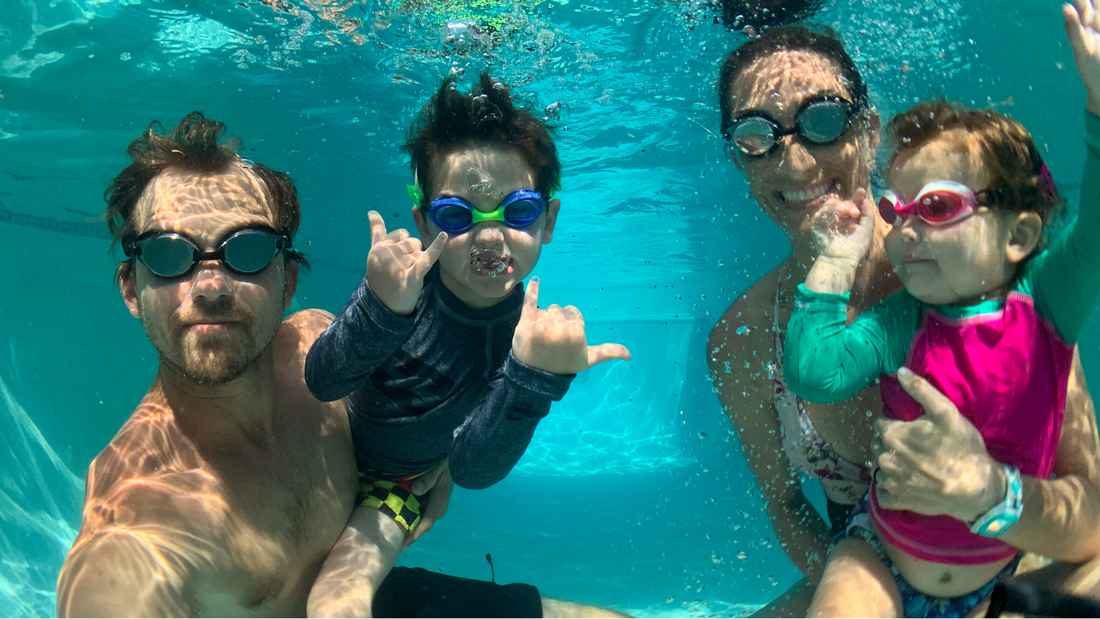 Family swimming underwater in pool wearing Frogglez swim goggles. Adult swim goggles and kids swim goggles for the whole family. Comfortable swimming goggles for curly hair. Toddlers and children swimming lessons in backyard pool.