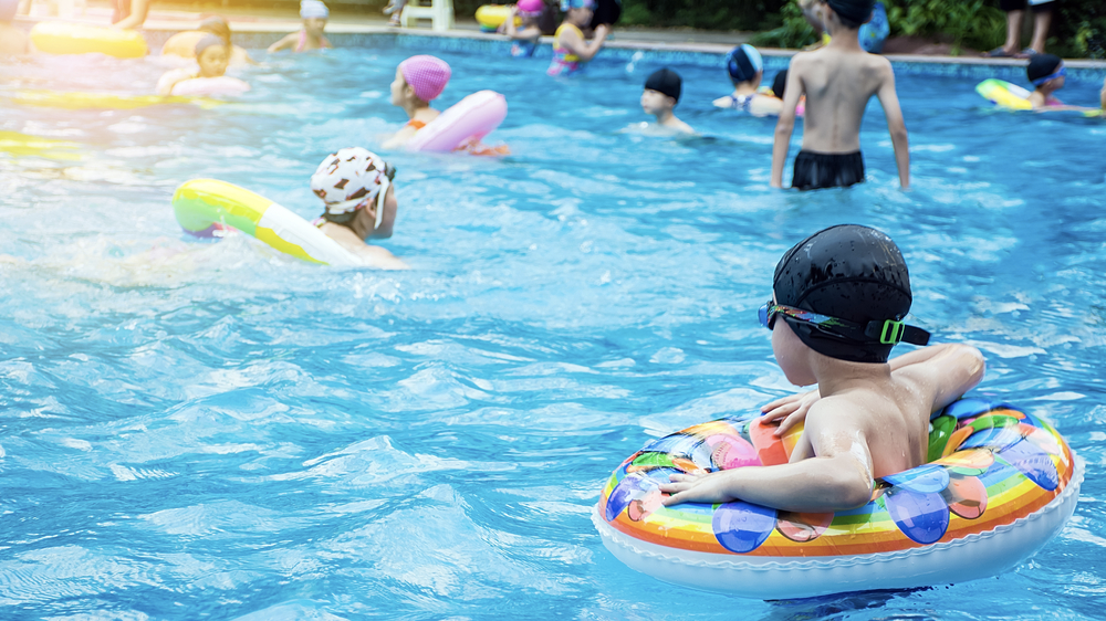 boy sitting alone on edge of swimming pool wrapped in a blue towel wearing blue Frogglez swim goggles. Frogglez comfortable neoprene strap won't pull hair. Best swim goggles for boys. Best swim goggles for girls.