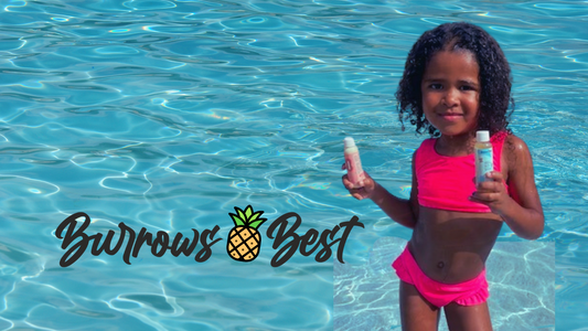 smiling Black girl wearing an orange bikini standing in the swimming pool holding Burrows Best after-swim products for kids